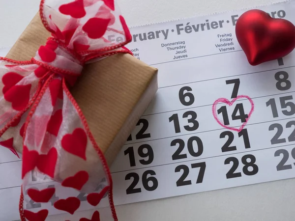 Calendar page with highlighted heart written in red on February 14 of Valentine\'s Day with red heart combination, gift box. Top view with space for greetings. Concept of Valentine\'s day, holiday