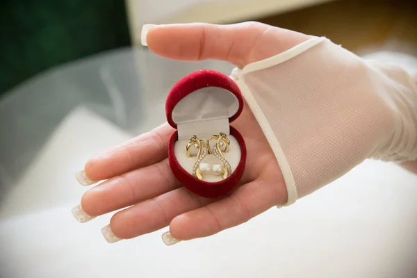 The bride holds a box of gold earrings in her hand. Red box with earrings