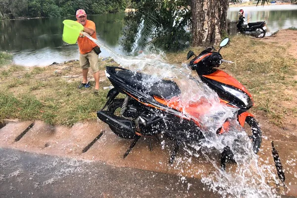 Wassen van een groene emmer van een oranje scooter naast een meer — Stockfoto