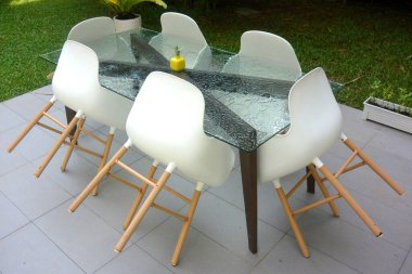 Yağmurdan sonra terasta ıslak cam masa ve altı beyaz sandalye.