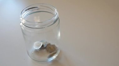 Beyaz arka planlı cam bir kavanoza düşen iki euro sikke.