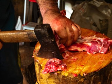 Kana bulanmış tahta bir kütükte beyaz domuz eti kesen bir işçi.