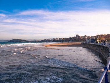 Sardinero sahili manzarası ve arka planda Magdalena sarayı ve gün batımında bulutları olan güzel bir gökyüzü.