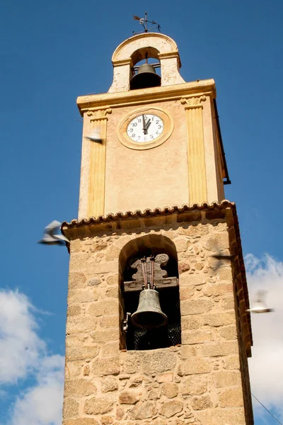 Tower with bell tower and weather vane in the highest part and clock marking one o\'clock, surrounded by flying pigeons