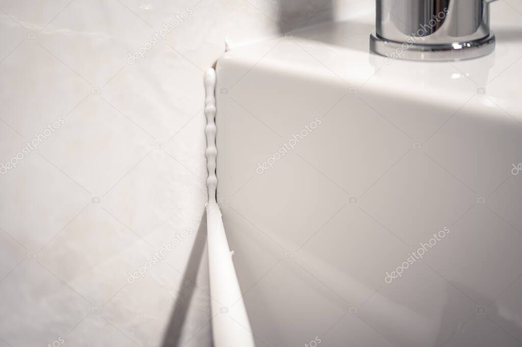 Detail of a cannula applying silicone to the seal of a bathroom sink