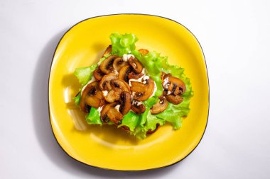 Yeşil yapraklı ekmek tostu kızarmış mantar salatası ve beyaz arka planda sarı tabakta beyaz sos.