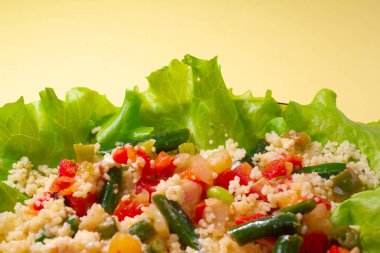 Sarı arka planda sarı tabakta marul ve sebzeli kuskus lapası sağlıklı fitness yemeği. Boşluğu kopyala