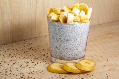 Sağlıklı kahvaltıda chia yoğurdu ve muz tohumları ahşap arka plan fitness yiyeceğinde. Boşluğu kopyala