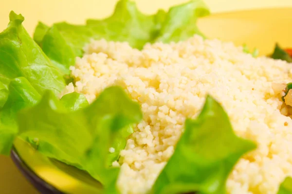 couscous porridge with lettuce and healthy fitness food on a yellow background. copy space