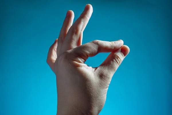 male hand shows ok finger sign on blue background copy space close up
