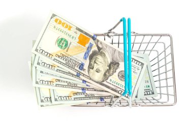 Beyaz arkaplandaki 100 dolarlık banknotlara mavi eklenmiş bir sepet yerleştiriliyor. izole et