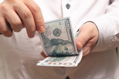 Kafkasyalı adam ofiste beyaz gömlekle 100 dolarlık banknotlar sayıyor.