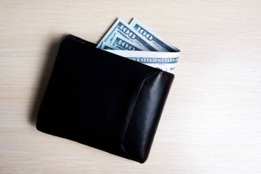 Açık ahşap arka planda siyah deri cüzdan içinde bir tomar dolar. Yukarıdan bak. kapatılacak