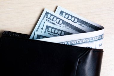 Açık ahşap arka planda siyah deri cüzdan içinde bir tomar dolar. Yukarıdan bak. kapatılacak