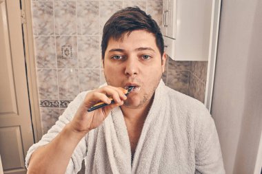 Beyaz önlüklü bir adam banyoda dişlerini fırçalıyor..