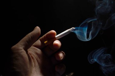 Siyah arka plan fotokopi alanında yanan bir sigarayı elle tut. Kapat.