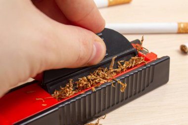 Sigara ve sigarayı arka planda hafif bir tahta üzerine doldurmak için bir makineye takılır.