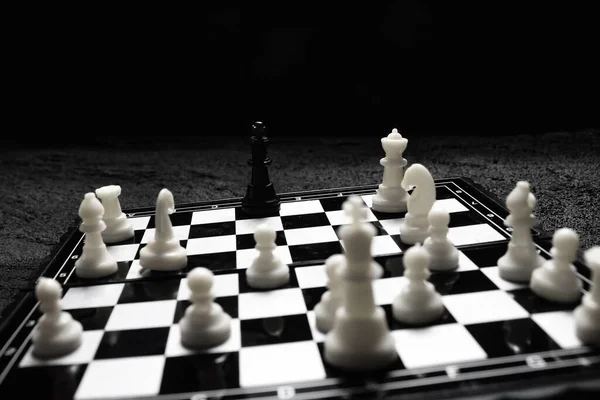 chessboard black king surrounded by enemies ambush on black concrete dark background .copy space