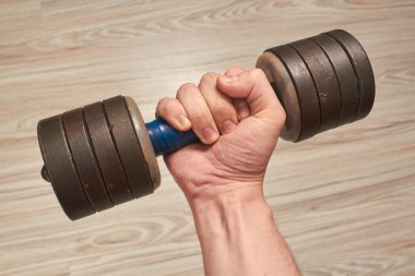 Erkek el evde, karantinada hafif ahşap parke arka planında bir dambıl tutuyor.