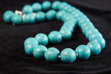 Siyah kadife üzerine yarı değerli turkuaz taştan boncuklar. Kapat.