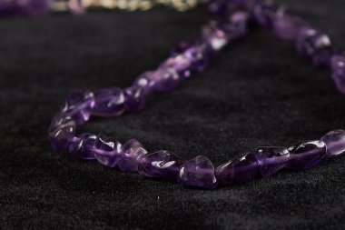 Siyah kadife üzerinde yarı değerli bir taş olan ametist kırıntılarından boncuklar. Kapat.