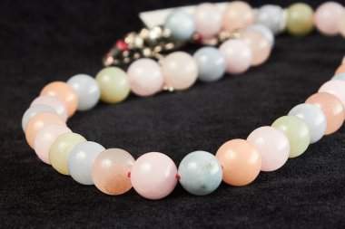 Siyah kadife üzerinde gül kuvars yarı değerli taştan boncuklar. Kapat.