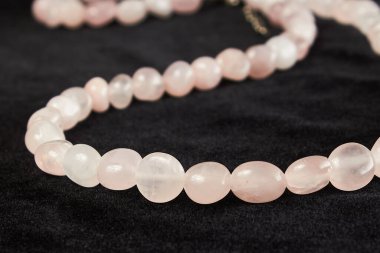 Siyah kadife üzerinde gül kuvars yarı değerli taştan boncuklar. Kapat.