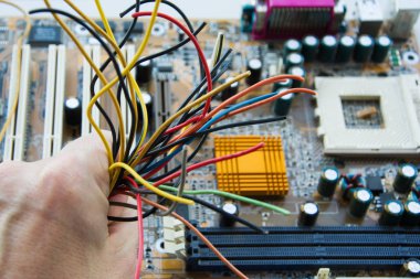 Bir adam elinde bilgisayarın arka planında farklı renklerde bir koşum takımı tutuyor. Hatalı bilgisayar ekipmanlarının onarımı ve elektronik aletlerin sorun giderilmesi kavramı