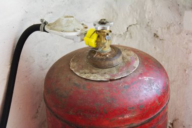 Kapakçık ve gaz hortumu olan eski kırmızı gaz tüpü duvarın yanında duruyordu.