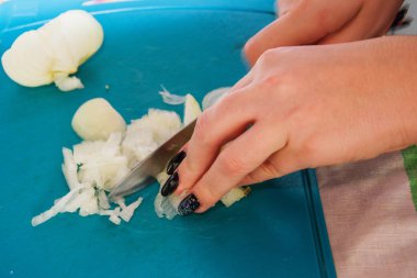 Güzel manikürlü bir kadın yeşil bir kesim tahtasındaki bıçakla soğan doğruyor..