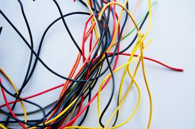 Farklı renklerdeki elektrik kablolarının çıkıntılı koşumları birbirine çok bağlıdır. Masanın beyaz arka planında kaos, karmaşa, karmaşa.