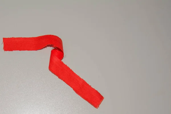 Zkroucená červená tkanina stuha s roztřepenými okraji a vyčnívajícími nitěmi na bílém pozadí. — Stock fotografie