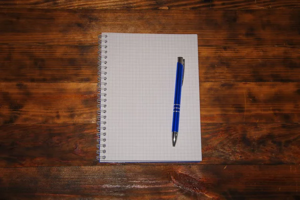 Draufsicht auf ein offenes leeres weißes Notizbuch mit blauem Stift auf dunklem rustikalem Holzgrund, Schulheft mit Spiralfeder, Schreibblock mit niedriger Schlüsselszene. — Stockfoto