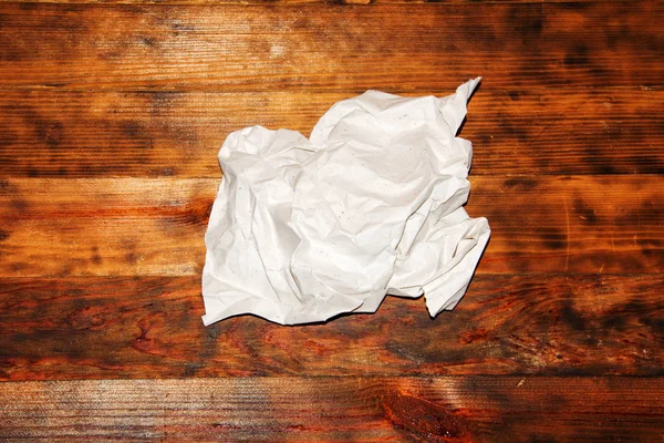 A crumpled sheet of white paper on a dark wooden background. Copy space for inscription.