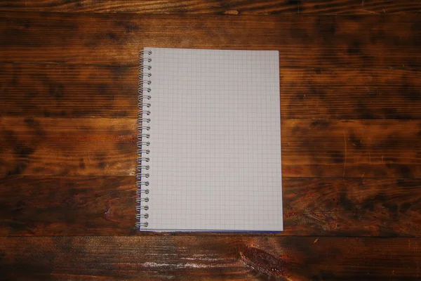 Top kilátás egy nyitott üres fehér notebook sötét rusztikus fa háttér, iskolai notebook spirál rugó, irodai jegyzettömb alacsony kulccsal jelenet. — Stock Fotó