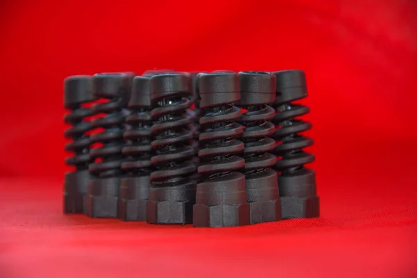 Plástico preto e peças de borracha de fabricação automotiva por injeção de molde de alta precisão na fábrica industrial. Peça de reposição na forma de uma mola espiral na superfície vermelha . — Fotografia de Stock