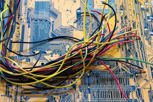 El manojo de cables eléctricos de diferentes colores están muy entrelazados en el fondo de la placa base PCB . —  Fotos de Stock