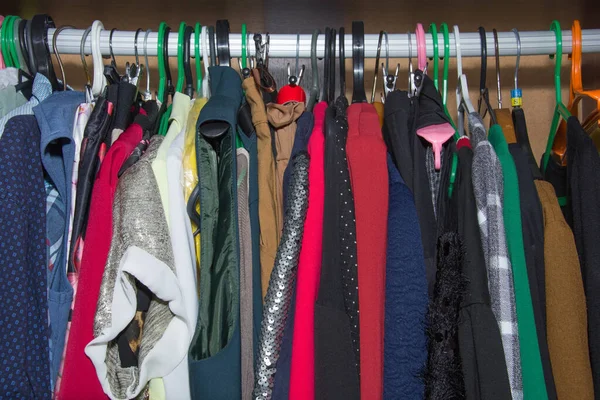 Шкаф с одеждой, висящей на разных цветных вешалках. Красочная одежда, висящая на перилах в деревянном шкафу . — стоковое фото