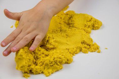 Çocukların elleri beyaz bir masada sarı kinetik kum oynuyor. Stres önleyici