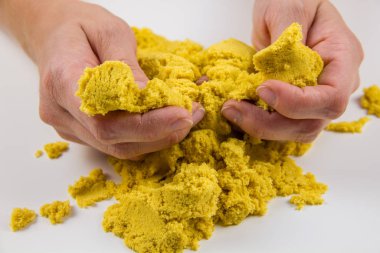 Kadın elleri beyaz bir masada sarı kinetik kum oynuyor.