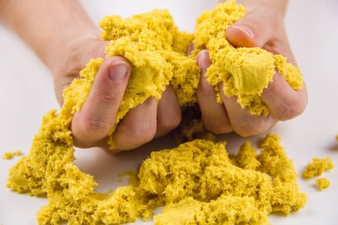 Kadın elleri beyaz bir masada sarı kinetik kum oynuyor.