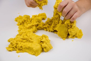 Çocukların elleri beyaz bir masada sarı kinetik kum oynuyor. Stres önleyici