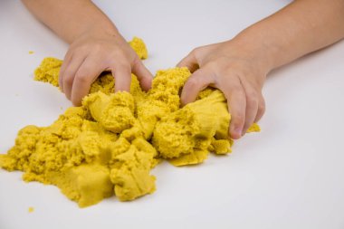 Çocukların elleri beyaz bir masada sarı kinetik kum oynuyor. Stres önleyici