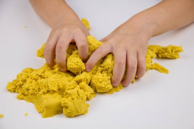 Çocukların elleri beyaz bir masada sarı kinetik kum oynuyor. Stres önleyici