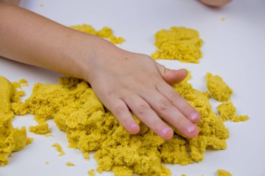 Çocukların elleri beyaz bir masada sarı kinetik kum oynuyor. Stres önleyici