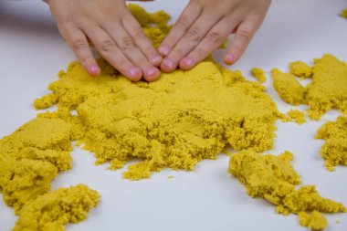 Çocukların elleri beyaz bir masada sarı kinetik kum oynuyor. Stres önleyici