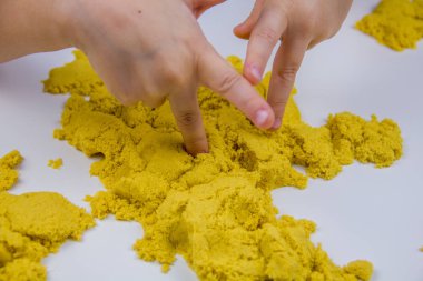 Çocukların elleri beyaz bir masada sarı kinetik kum oynuyor. Stres önleyici