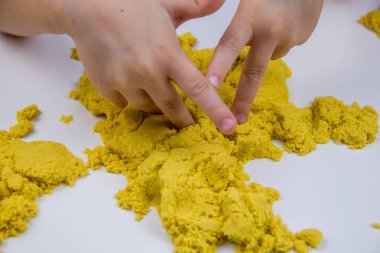 Çocukların elleri beyaz bir masada sarı kinetik kum oynuyor. Stres önleyici