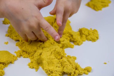 Çocukların elleri beyaz bir masada sarı kinetik kum oynuyor. Stres önleyici