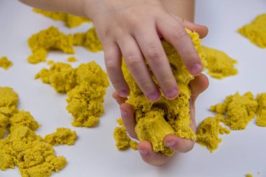 Çocukların elleri beyaz bir masada sarı kinetik kum oynuyor. Stres önleyici